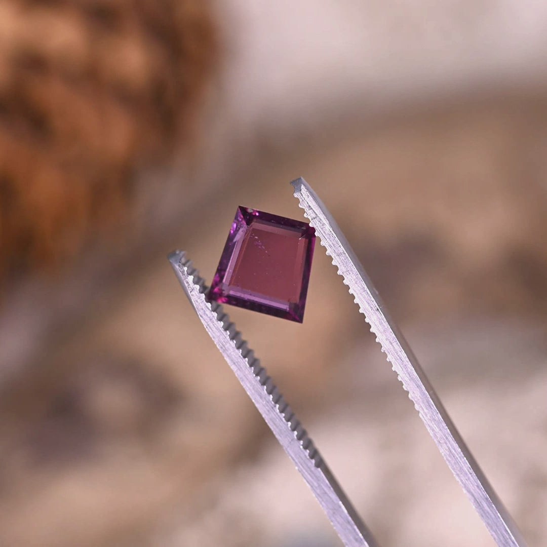 Rotating loose pink‑purple garnet from Kenya held in tweezers, showing the crisp step cut trapezoid tablet lines and the mirror-like flashes across the table.