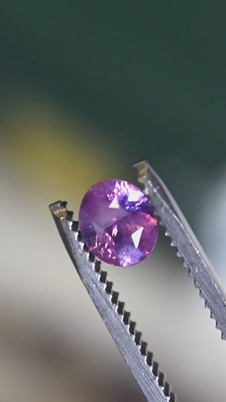 Precision oval mix cut sapphire turning in tweezers, highlighting opalescent glow and pastel purple pink saturation.