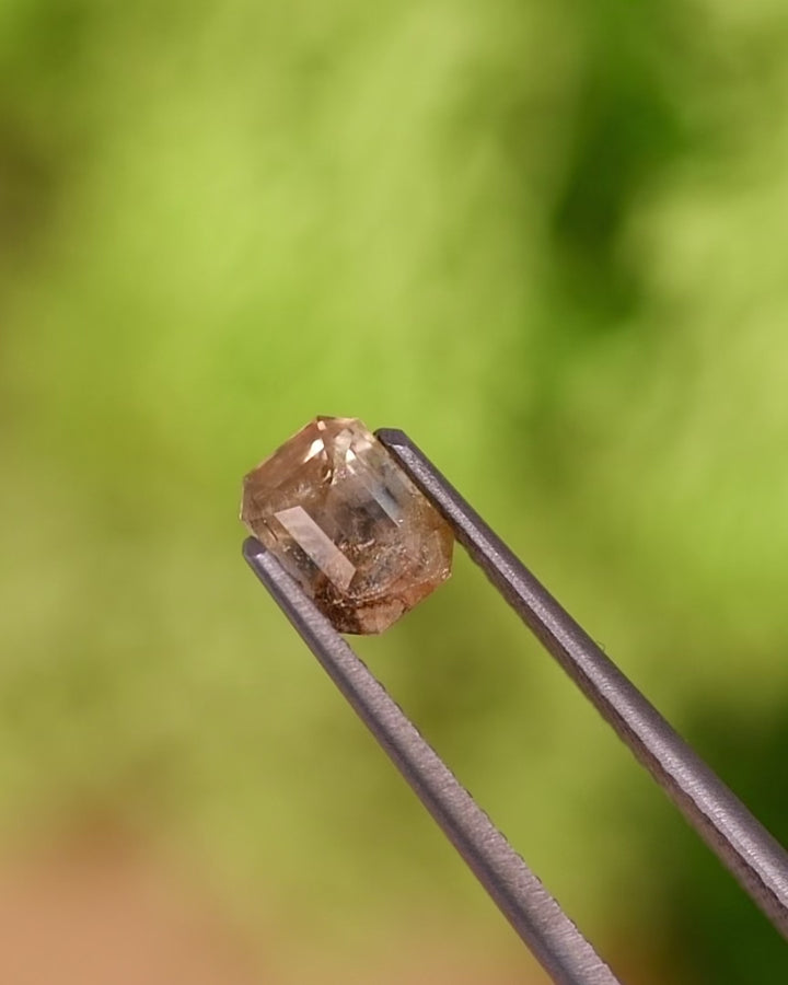 Video of 1.11CT grey teal yellow parti sapphire turning in tweezers, revealing natural color zones and brilliance of its custom emerald cut, untreated sapphire from Umba River Valley, Tanga, Tanzania.