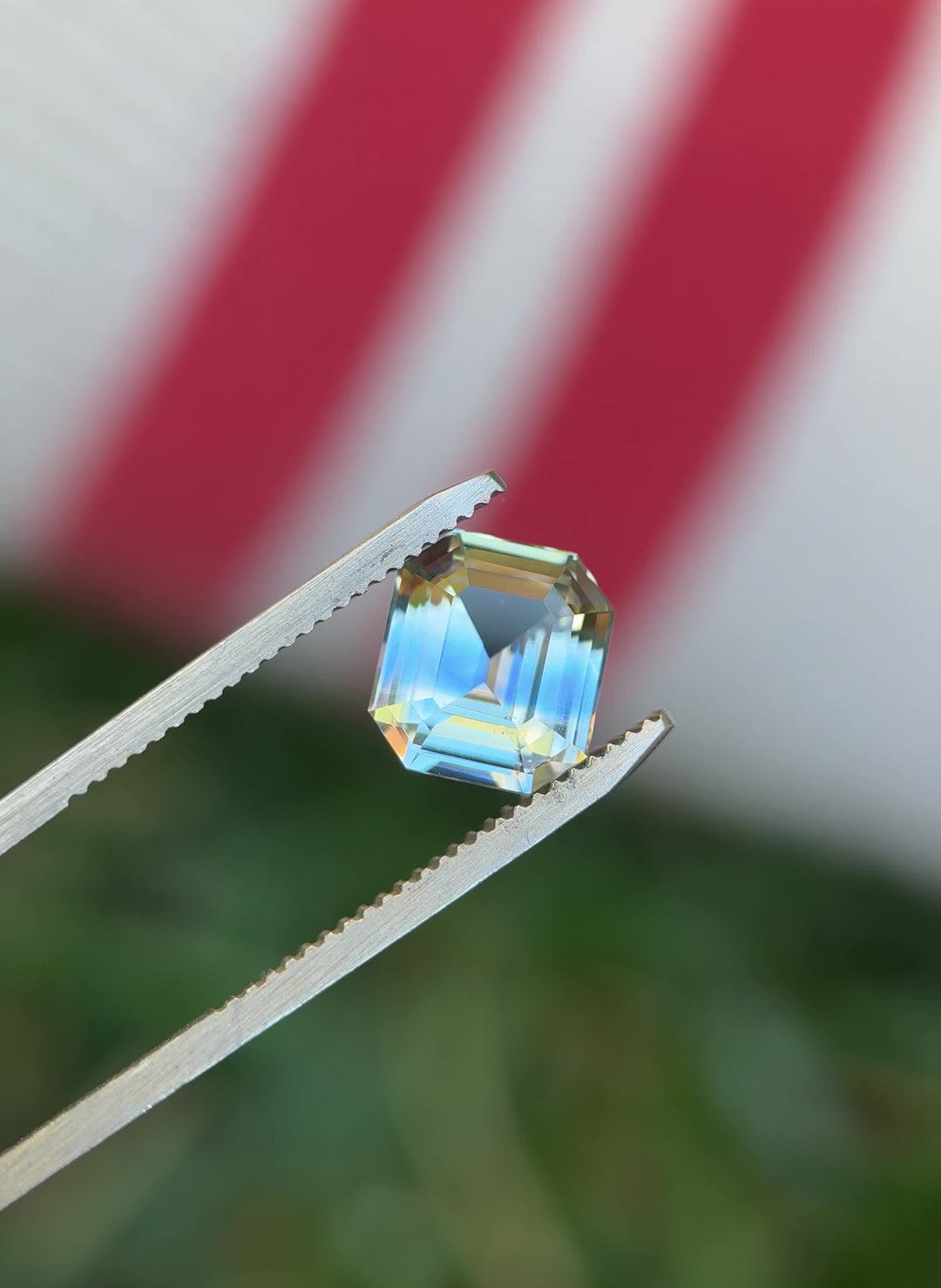 Video of a 4.04 carat light yellow and blue parti sapphire being rotated in gem tweezers, showing the precision emerald cut step facets and strong color zoning under natural lighting.