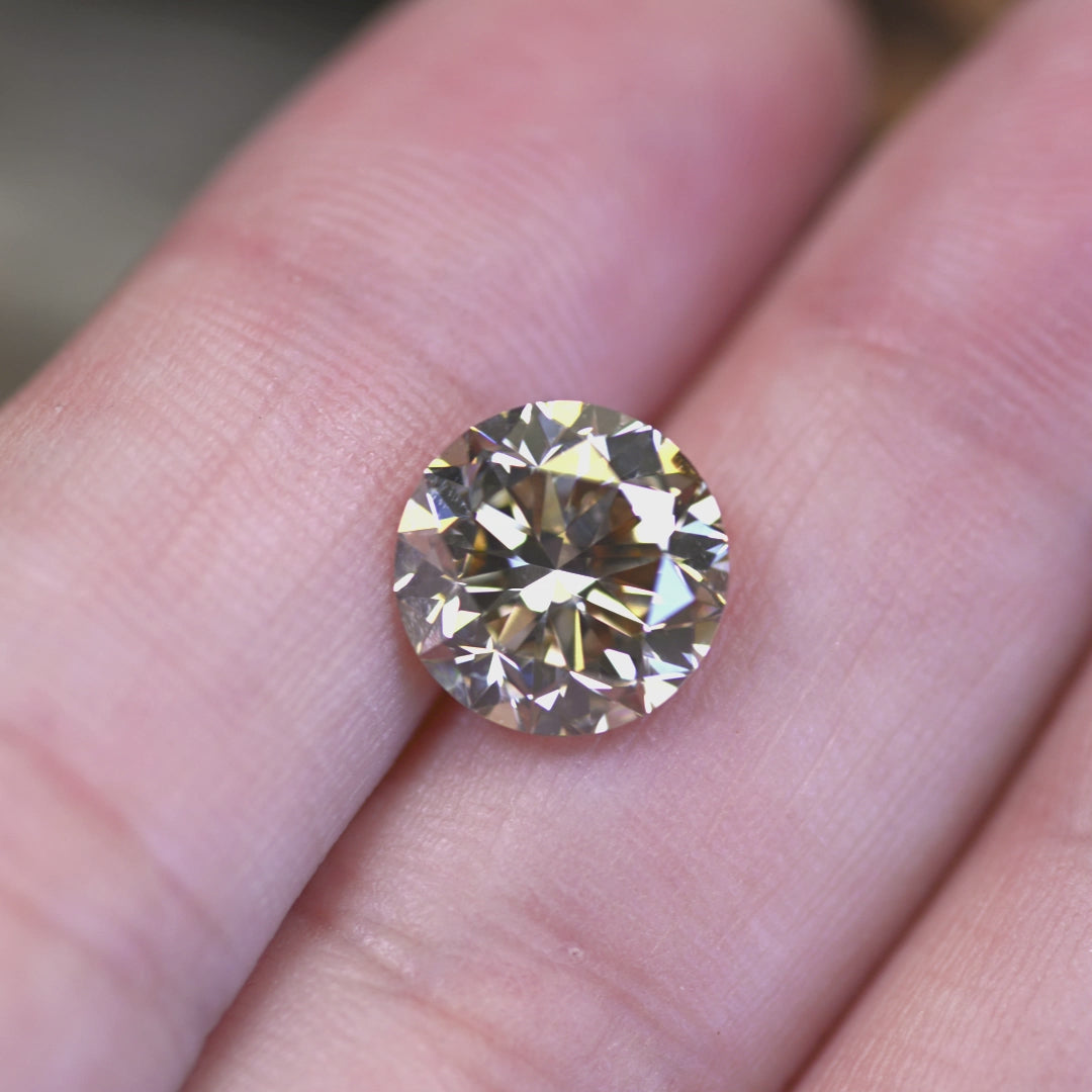 4.23ct C3 champagne round brilliant diamond rotated in hand, showing excellent cut sparkle and warm golden flashes.