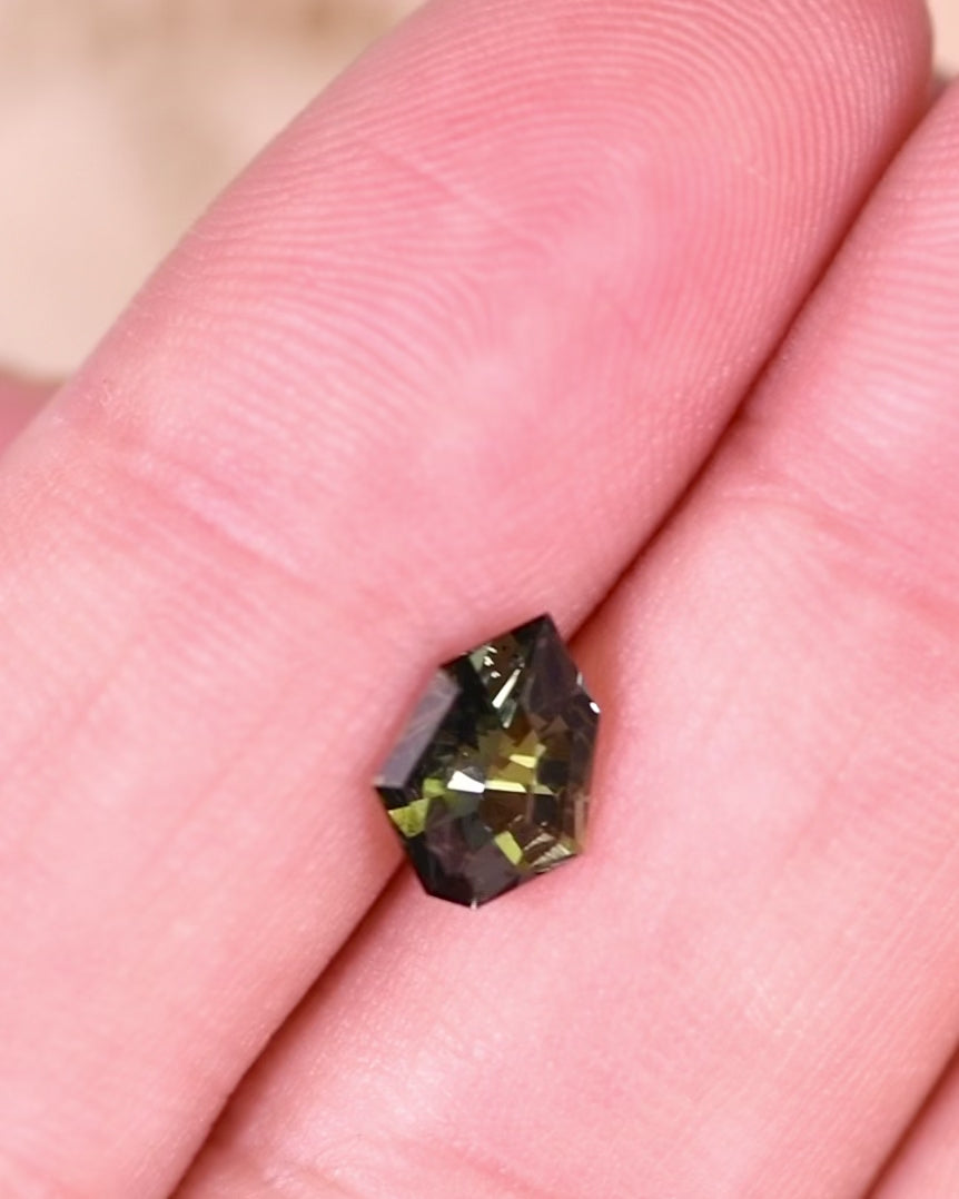 Macro video of 1.05 carat yellow green blue tanzanite turning under natural sunlight, emphasizing its vibrant tricolor brilliance and precision faceting of the custom geometric mix cut shield, untreated gem from Merelani Hills, Arusha Region, Tanzania.