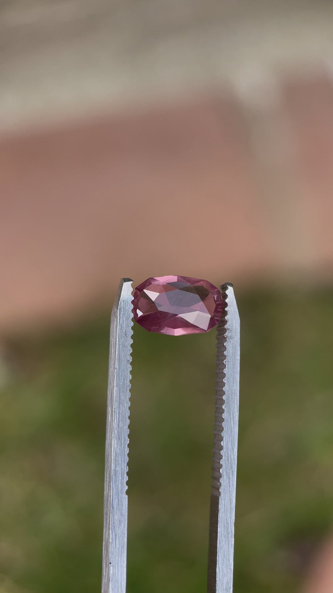 A delicate 1.45-carat grapefruit pastel sapphire with an elongated cushion cut, placed under precision lighting, showing its soft peach-pink hues and faceted brilliance.