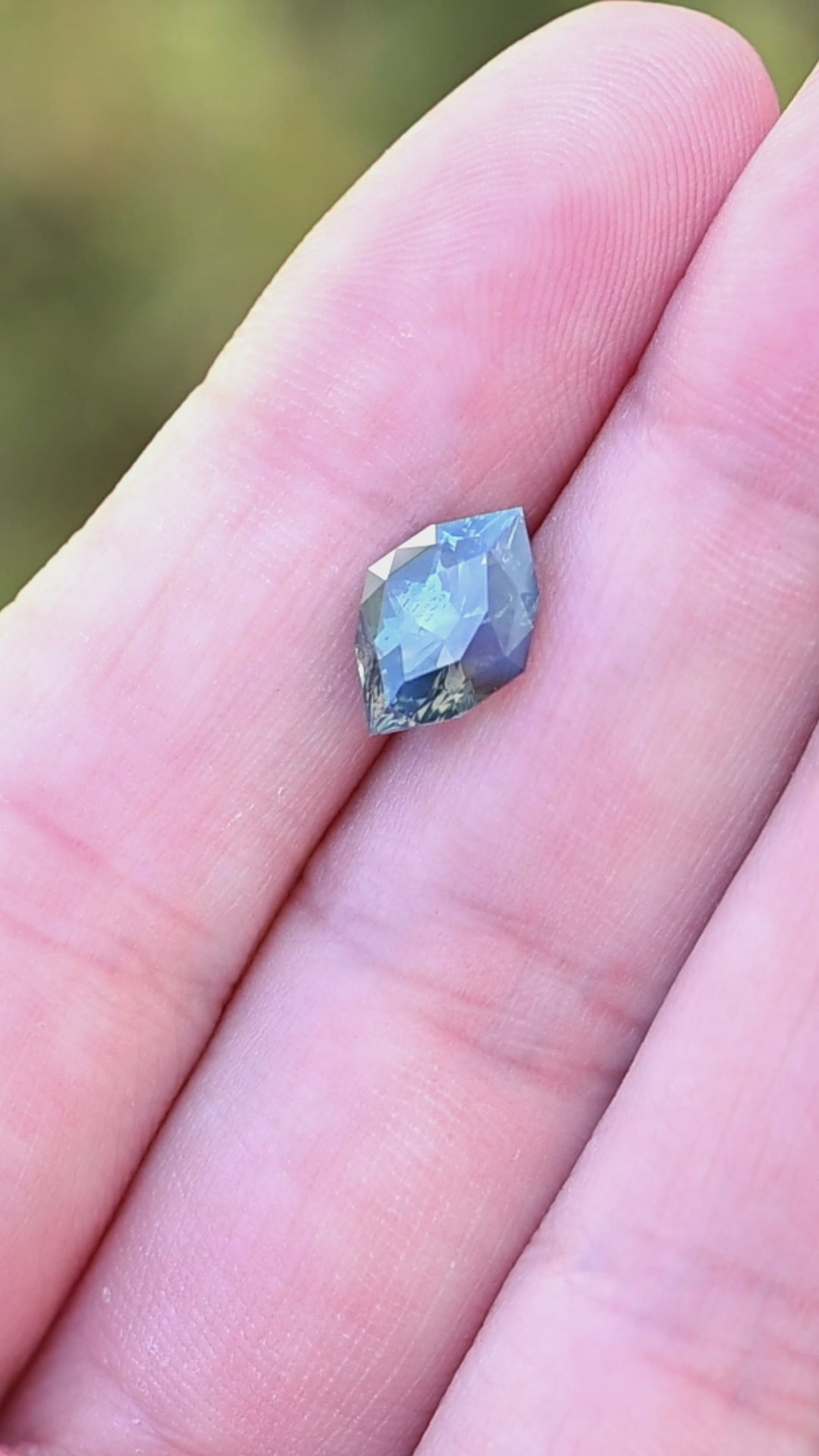 3.02ct opalescent teal parti marquise cut sapphire resting on fingertips rotating under natural light.