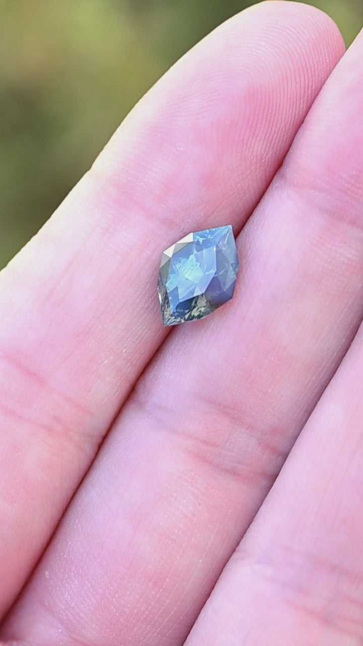 3.02ct opalescent teal parti marquise cut sapphire resting on fingertips rotating under natural light.
