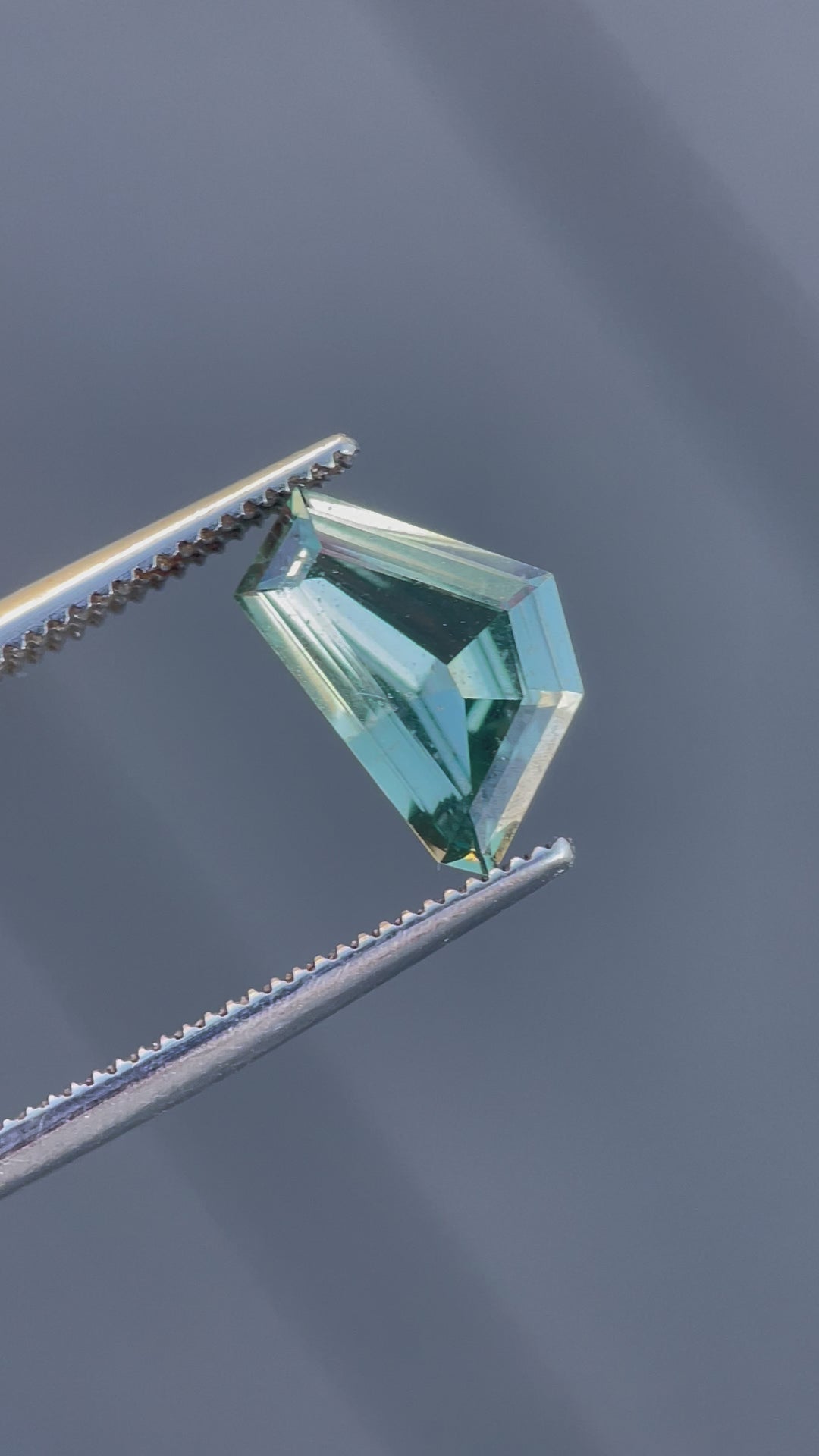 A handheld video featuring a geometric freeform sapphire weighing 2.00 carats, revealing its blue and green tones from various angles.
