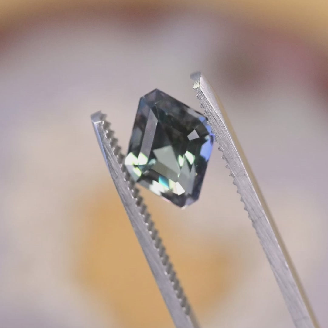 2.81 carat custom parallelogram step cut Tanzanite rotating under light showing mermaid violet blue teal green color play and sharp geometric faceting