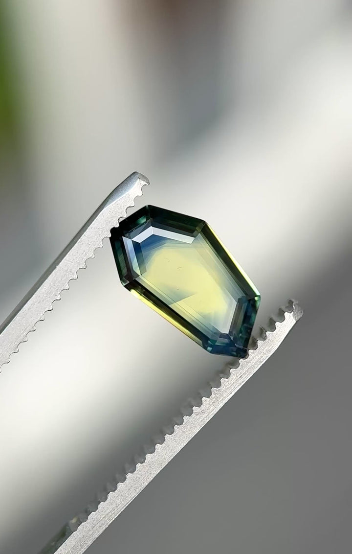 Parti sapphire rotating in natural light showing teal blue green and yellow color zoning and geometric shield cut.