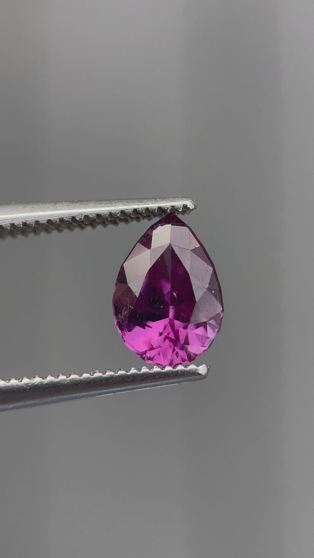 A short video featuring a pinkish-purple pear-shaped sapphire held between tweezers and shown from multiple angles.