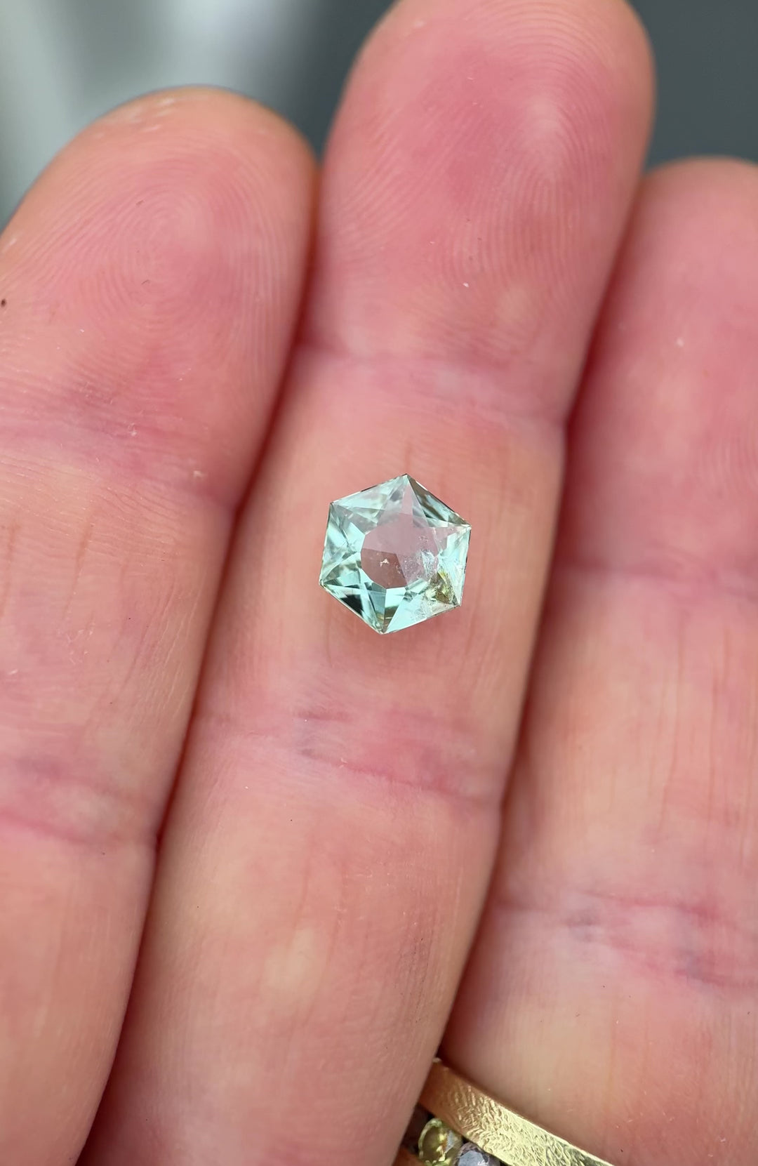 Close-up video of a precision cut Montana sapphire being gently tilted to show brilliance and facet geometry, featuring a mint sage teal green color, hexagon mixed cut, open culet, and untreated clarity