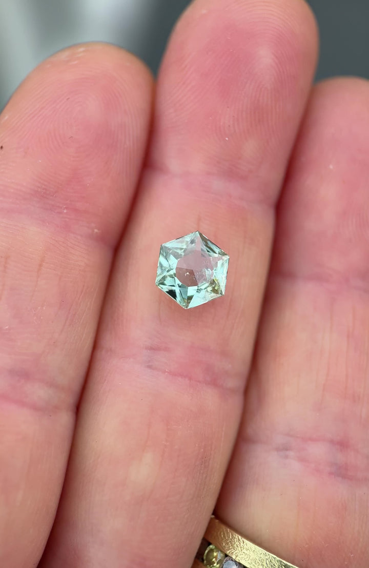 Close-up video of a precision cut Montana sapphire being gently tilted to show brilliance and facet geometry, featuring a mint sage teal green color, hexagon mixed cut, open culet, and untreated clarity