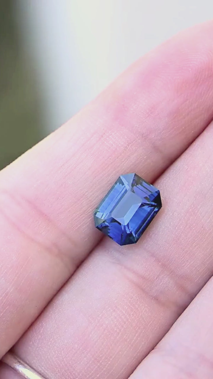 3.54 carat precision emerald-cut Madagascar sapphire moving on a hand, revealing shifts between saturated royal blue, cobalt blue and subtle teal in natural light.