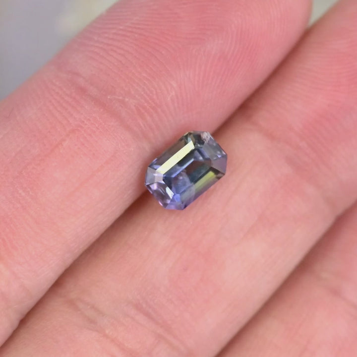 1.60 carat untreated teal green purple Tanzanite emerald cut rotating on hand under natural light, Merelani Hills Tanzania gemstone showing step cut brilliance and vivid color shift for custom jewelry