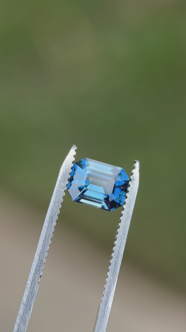 Precision emerald cut sapphire in tweezers showing depth, symmetry, and vivid teal blue tones in motion.