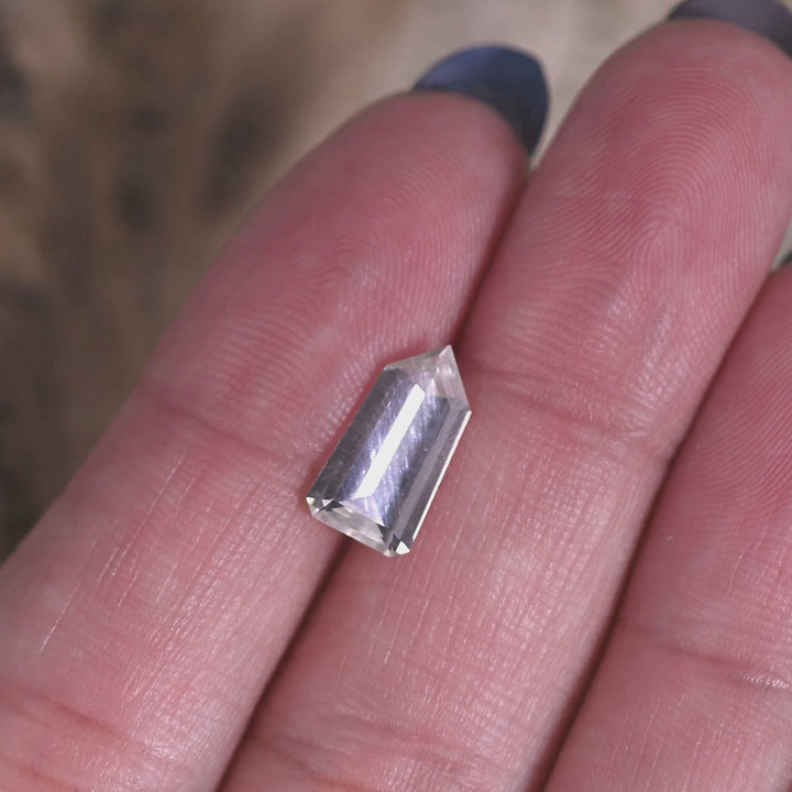Rotating loose 2.51ct light seafoam no-heat sapphire from Sri Lanka on the hand, showing the custom shield step cut as the stone shifts from icy blue-white to soft seafoam in the light.