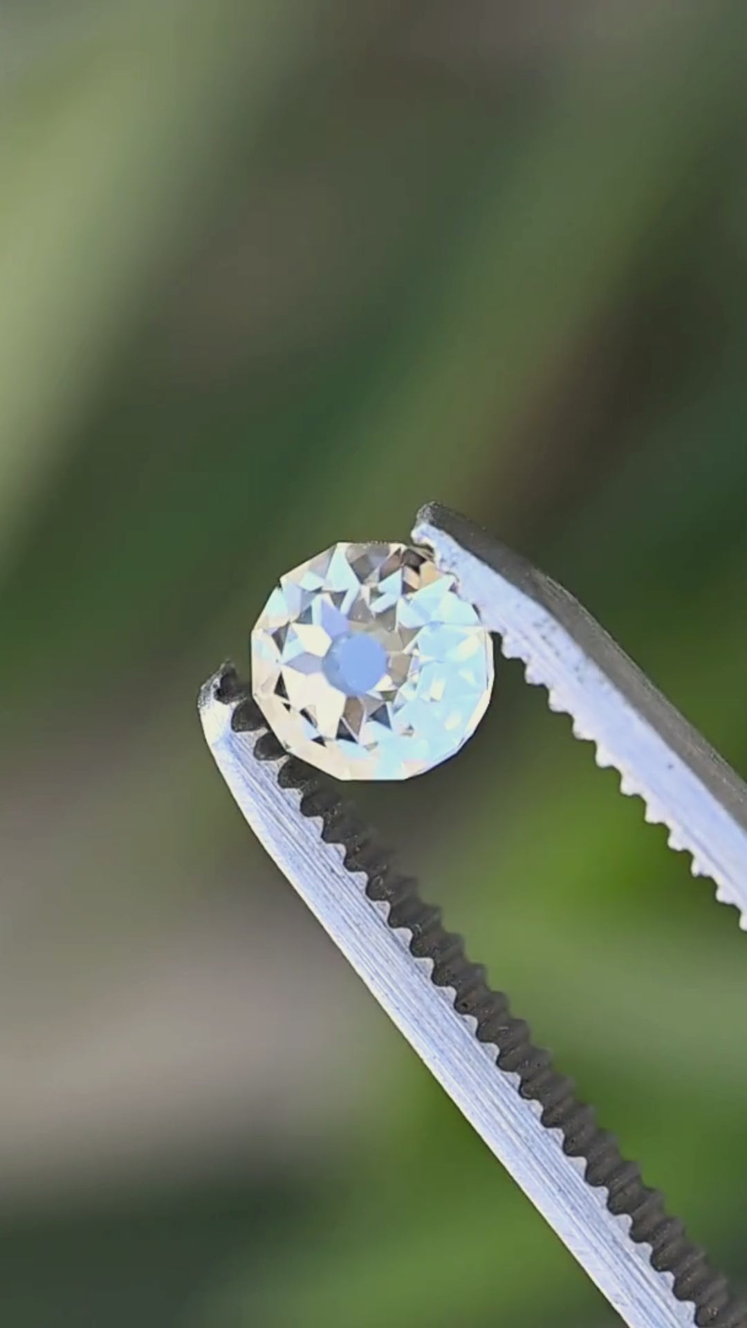 Round Mughal cut South African diamond rotated between jeweler’s tweezers, showing its dimensional profile and changing mosaic of reflections across the facets.