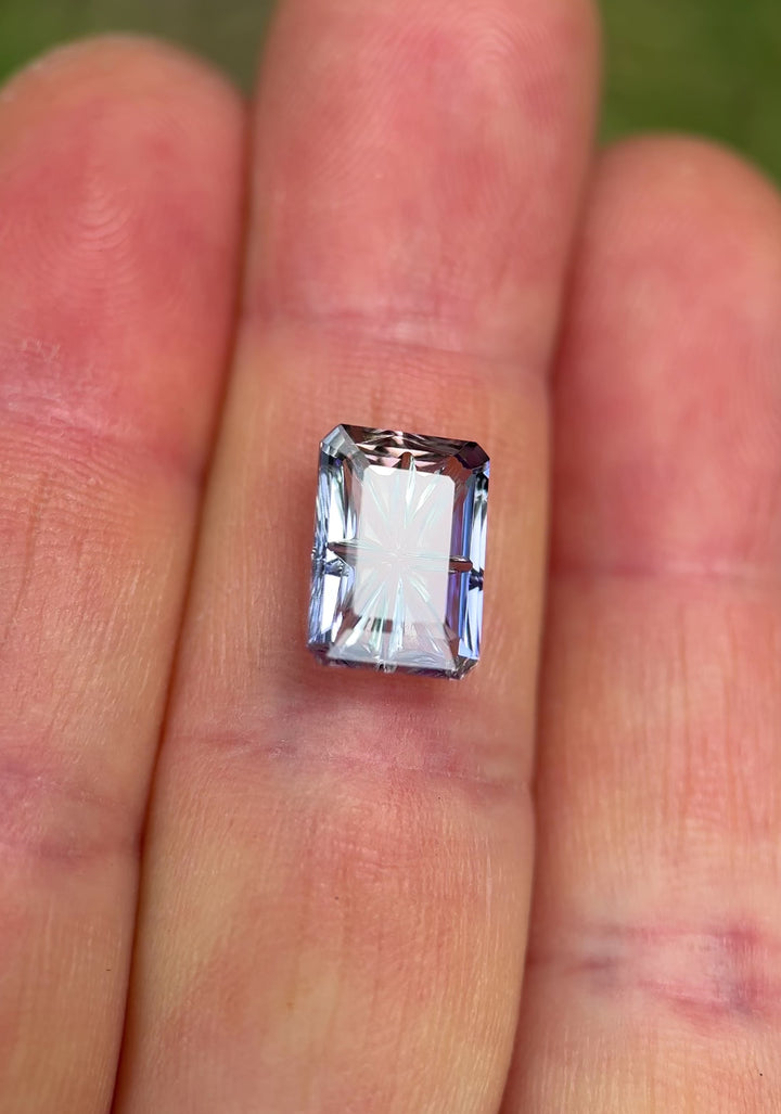 Rotating close-up video of a 4.01CT Tanzanite featuring blue, pink, and purple hues with a concave fantasy emerald cut. Stone is turned under natural light to show brilliance, color zoning, and portrait-style faceting.