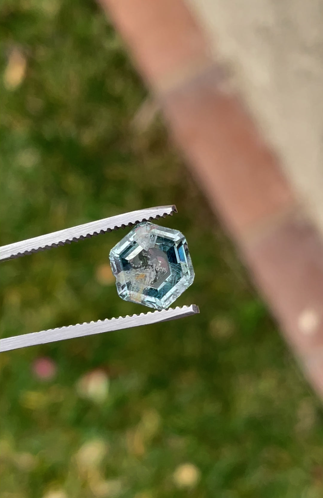 Video showcasing a 4.00 carat hexagon-shaped teal green sapphire, held in tweezers for a detailed view.