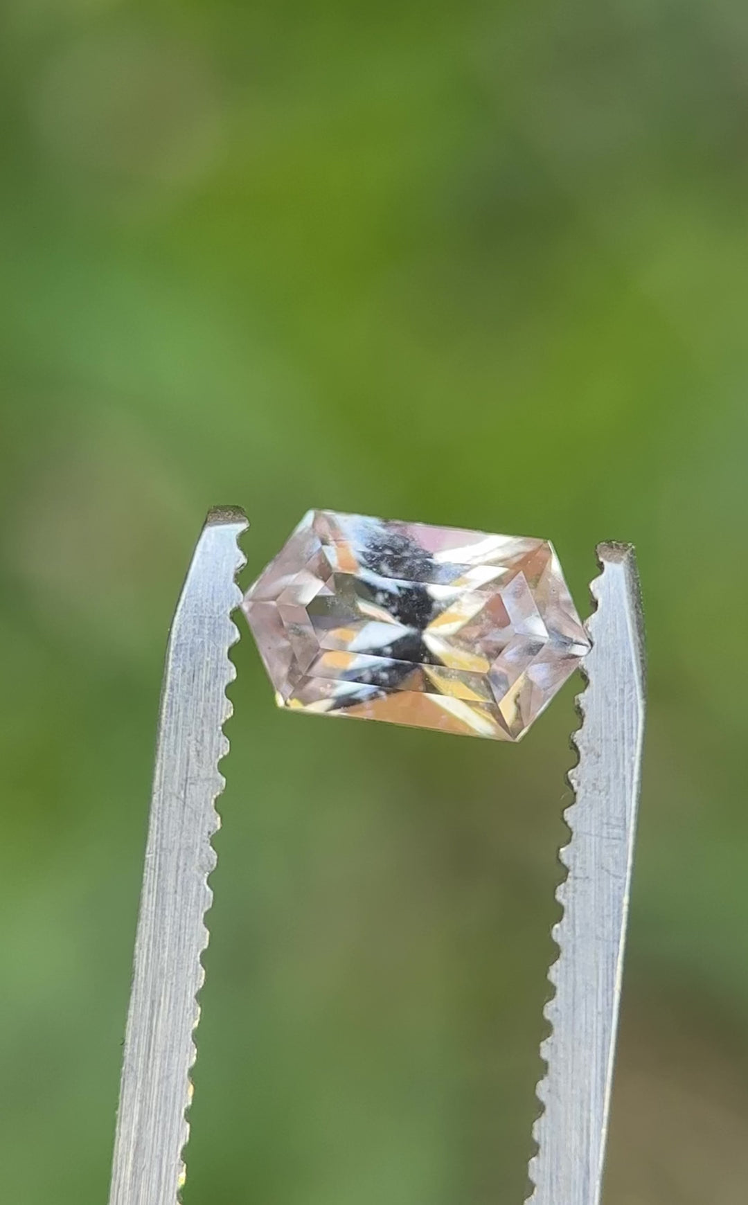 Rotating peach pink sapphire showing light performance and facet reflections in elongated hexagon cut.