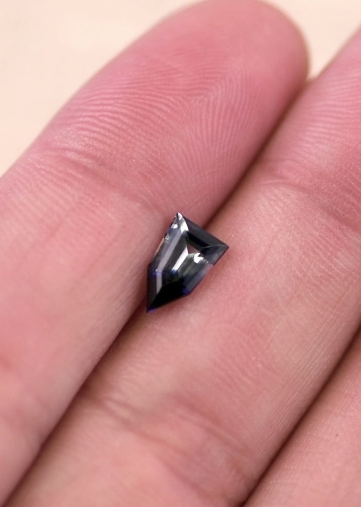 Handheld video of a bi-color colorless blue sapphire in natural light, highlighting pentagon shield step cut facets, crisp symmetry, and untreated origin from Ratnapura Sri Lanka
