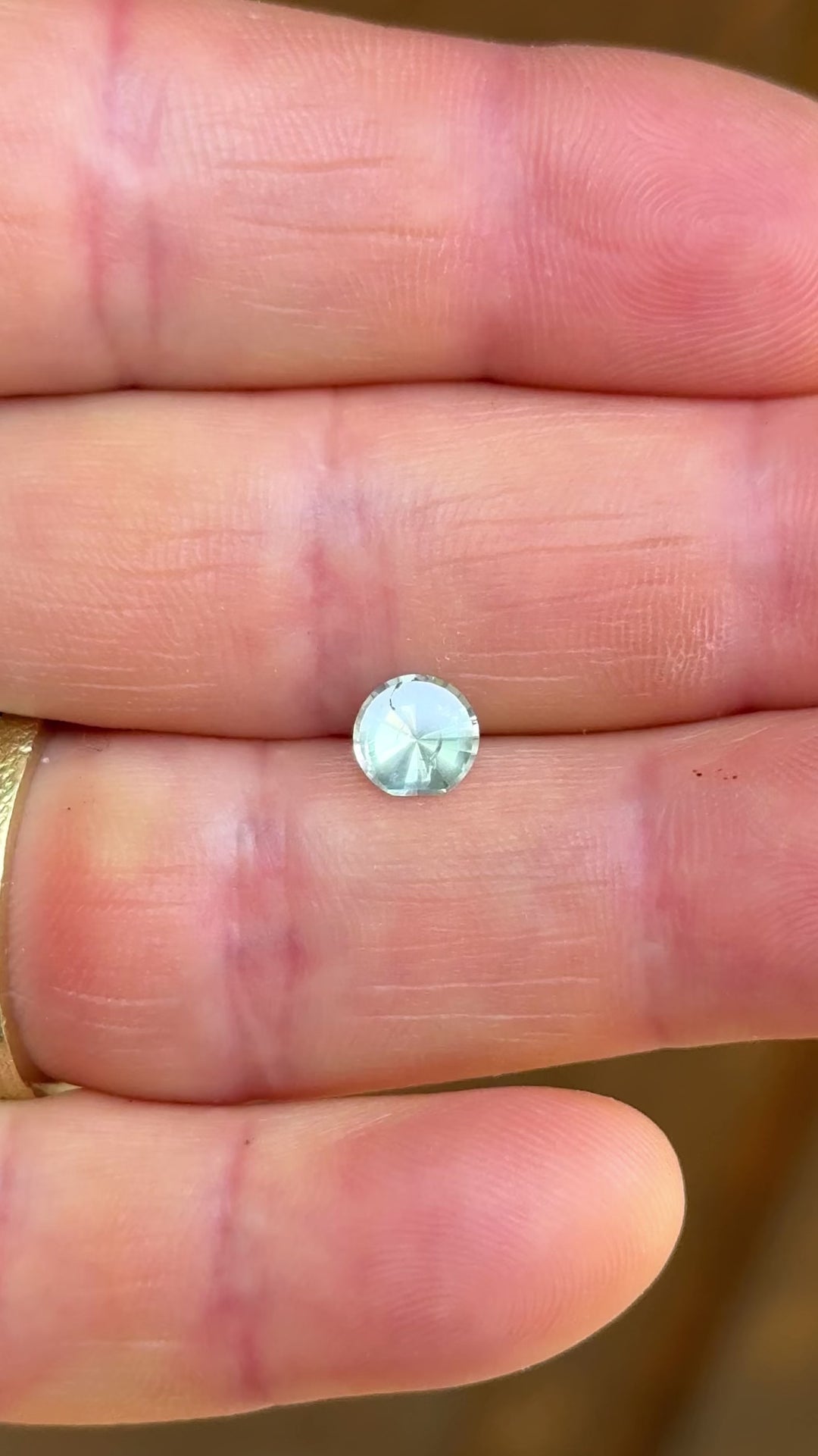 A rotating 0.96-carat seafoam sapphire shown from multiple angles in natural light, emphasizing the moon phase round cut and lively teal, yellow, and green color shifts.