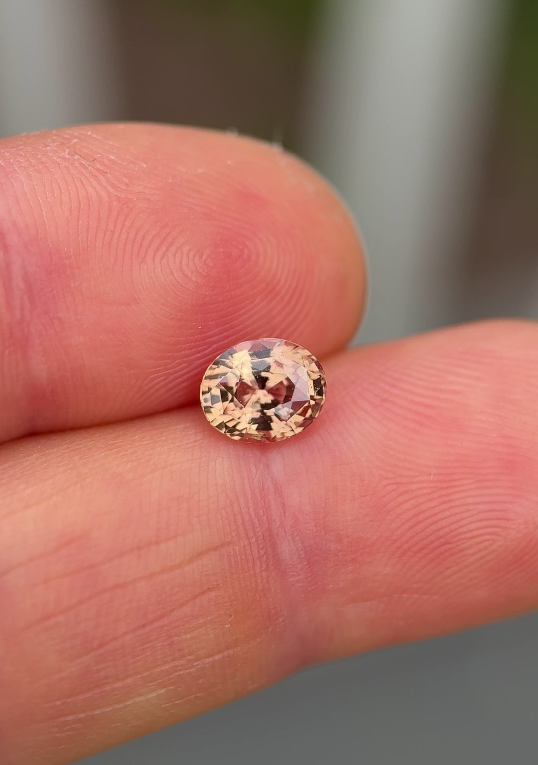 Natural light video of 1.51-carat unheated sapphire with peach and pink brilliance, resting on fingertip to highlight clarity and cut