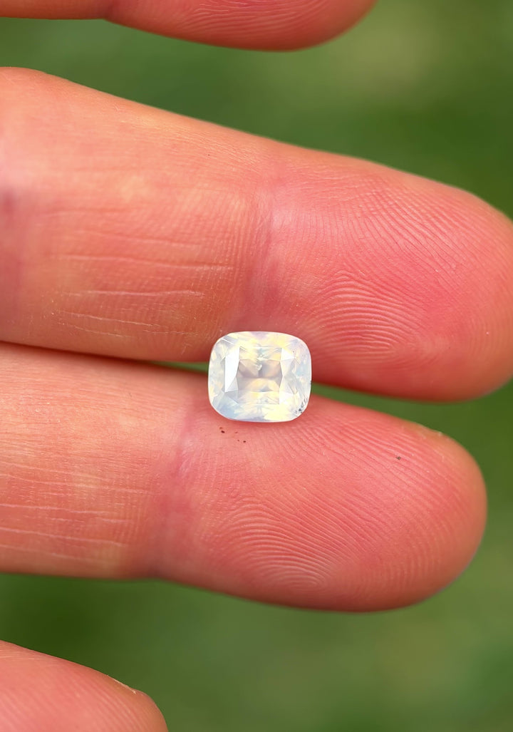 Close-up handheld video of natural 3.01CT opalescent white cushion cut sapphire from Ratnapura, Sri Lanka, revealing fine facet detail, brilliance, and soft internal glow.