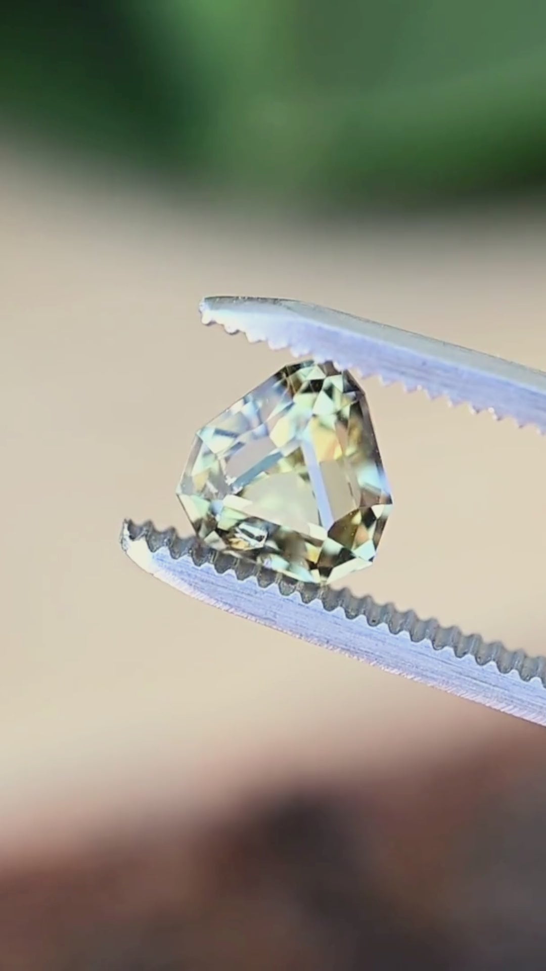 A custom geometric shield cut Tanzanite turning slowly in jeweler's tweezers, displaying crisp faceting, vibrant pleochroism, and dramatic flashes of teal, green, and yellow.