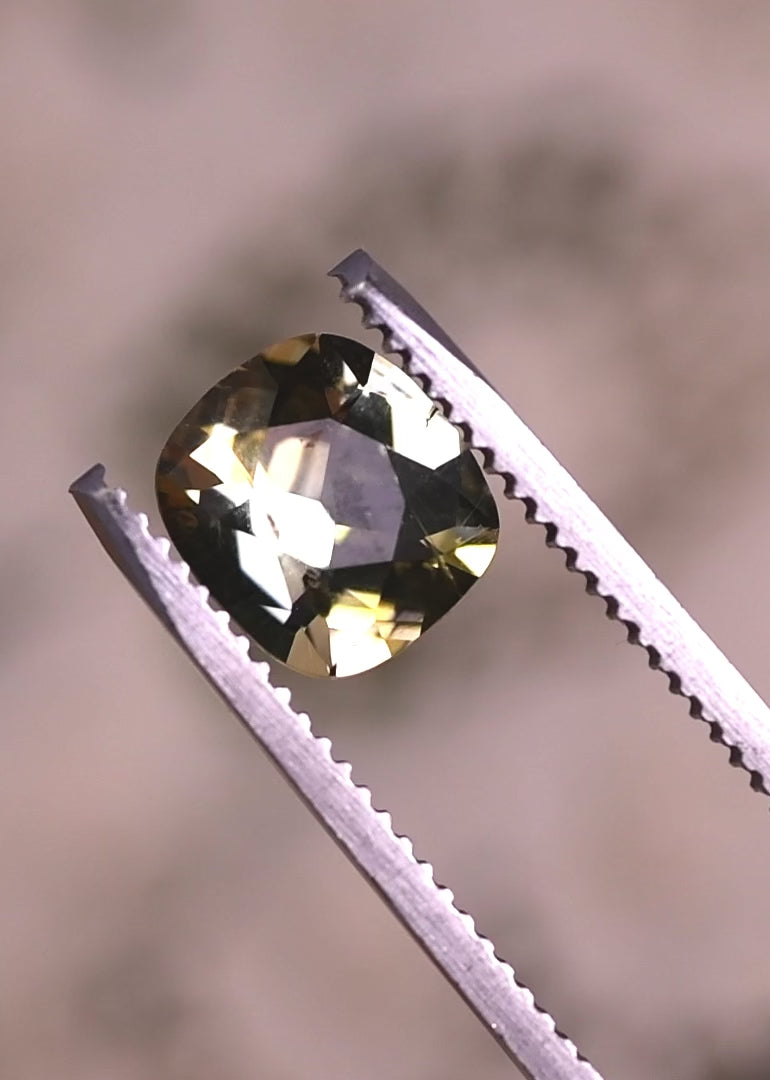 Close-up video of 2.17 carat yellow green Tanzanite cushion cut held in tweezers, showing depth, brilliance, and natural untreated crystal structure from Tanzania