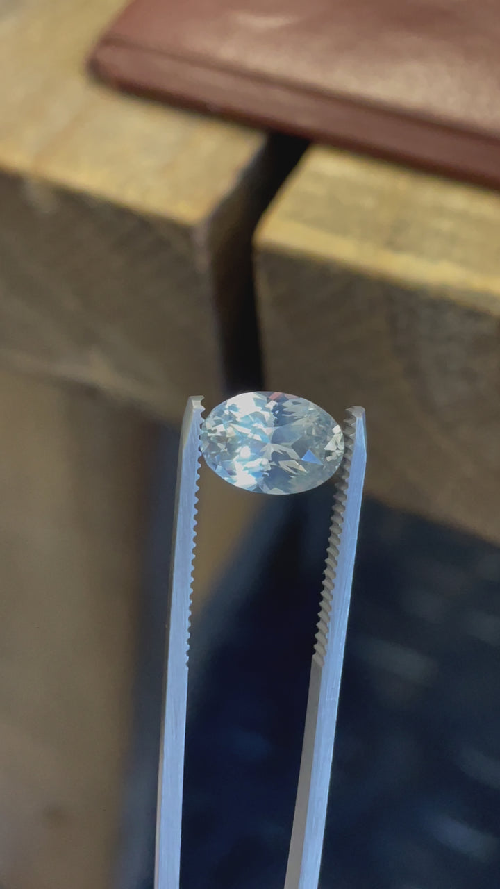 A 4.23-carat opalescent white sapphire in an oval brilliant cut, rotating to display its shimmering white and yellow hues from Sri Lanka.