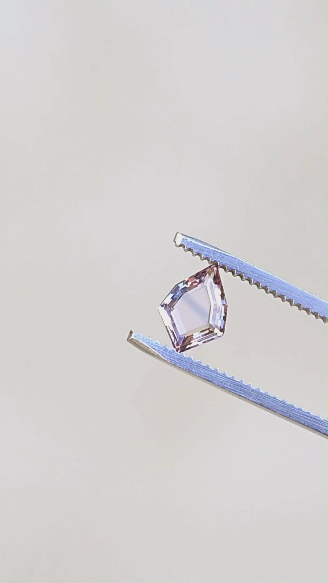 1.12ct peach and blue parti portrait cut sapphire rotating in gem tweezers in natural lighting.