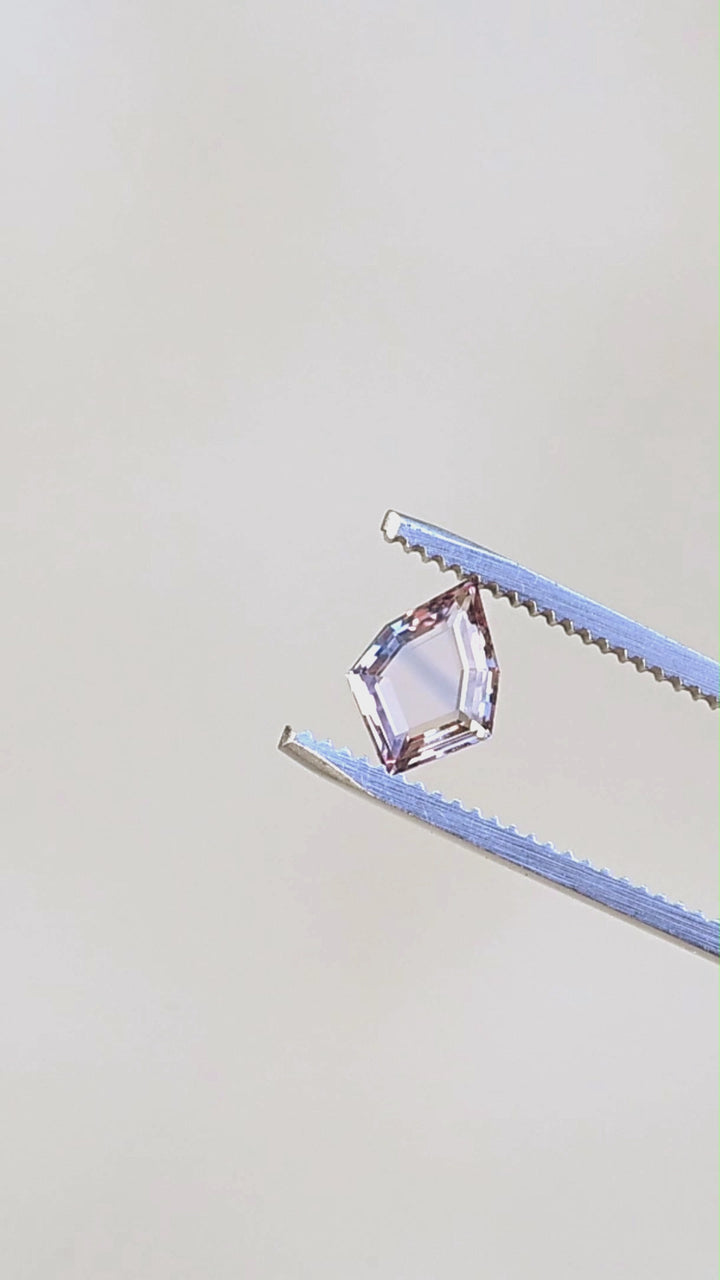 1.12ct peach and blue parti portrait cut sapphire rotating in gem tweezers in natural lighting.