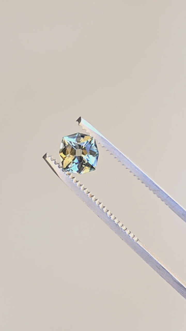 1.62ct teal yellow parti custom old mine cushion cut sapphire rotating in gem tweezers under natural light showing off natural parti color zoning.