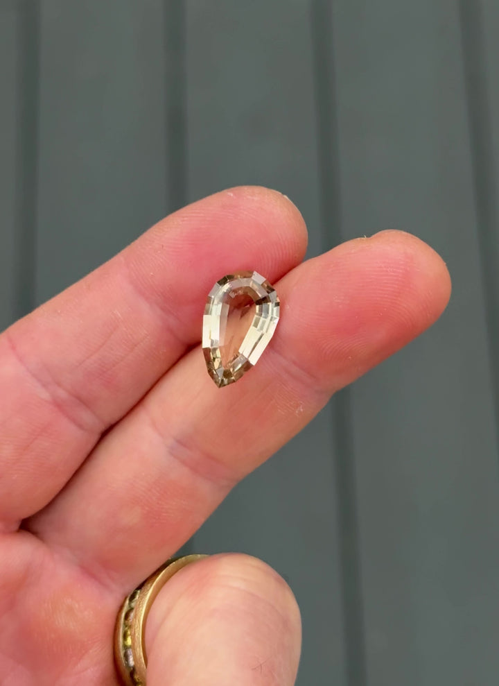 Macro close-up video of 5.36CT champagne brown tourmaline gemstone turning in hand, revealing its geometric pear step cut and natural warm champagne hue, mined ethically in Congo, Africa.