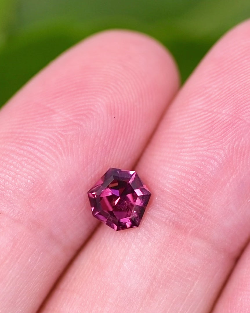 Macro video of 1.00 carat garnet turning slowly, revealing flashes of red, pink, and violet light through its geometric shield cut facets, natural unheated gem from Kenya.