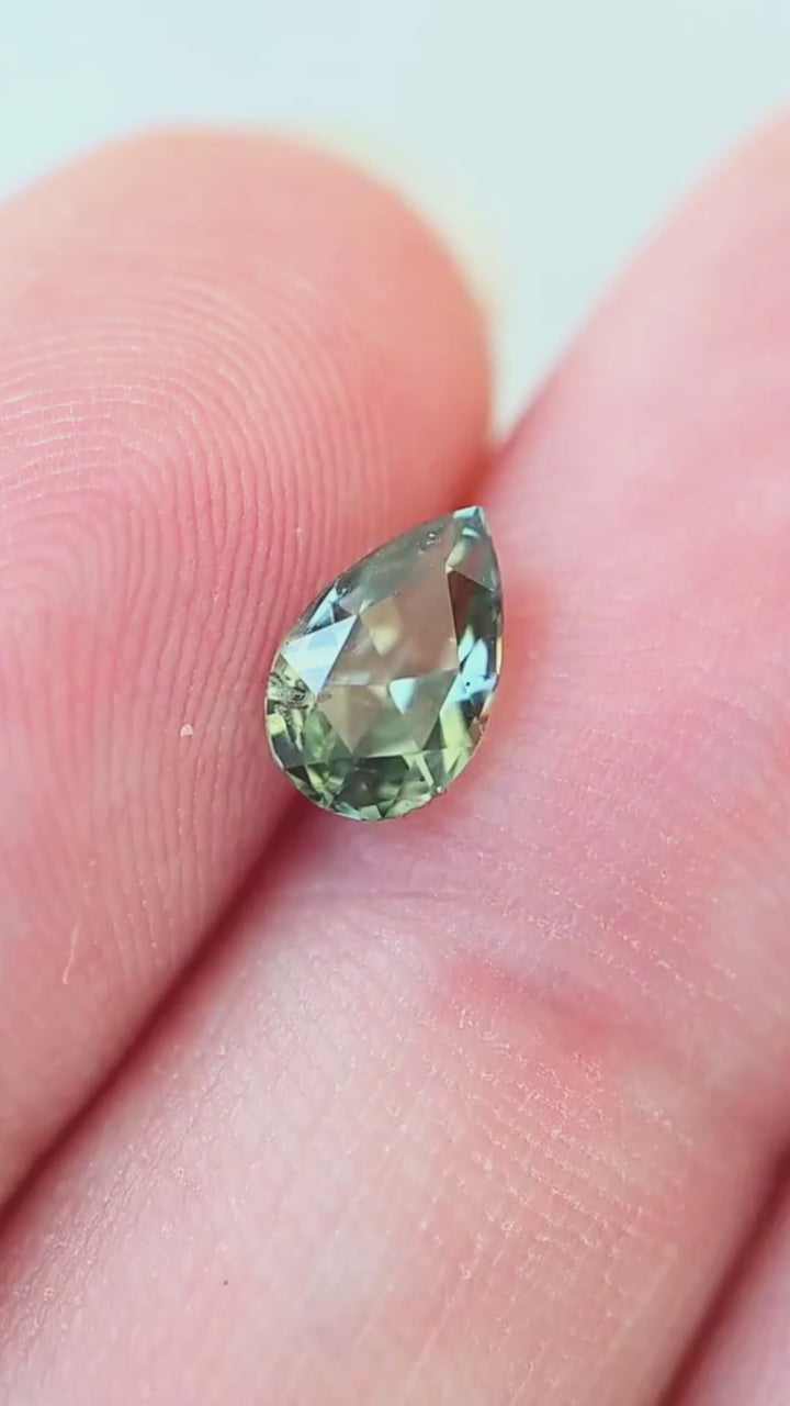 A hand-held view of this 1.01ct precision pear cut sapphire from Diego, Madagascar, showcasing its proportions and layered forest green and teal coloration.