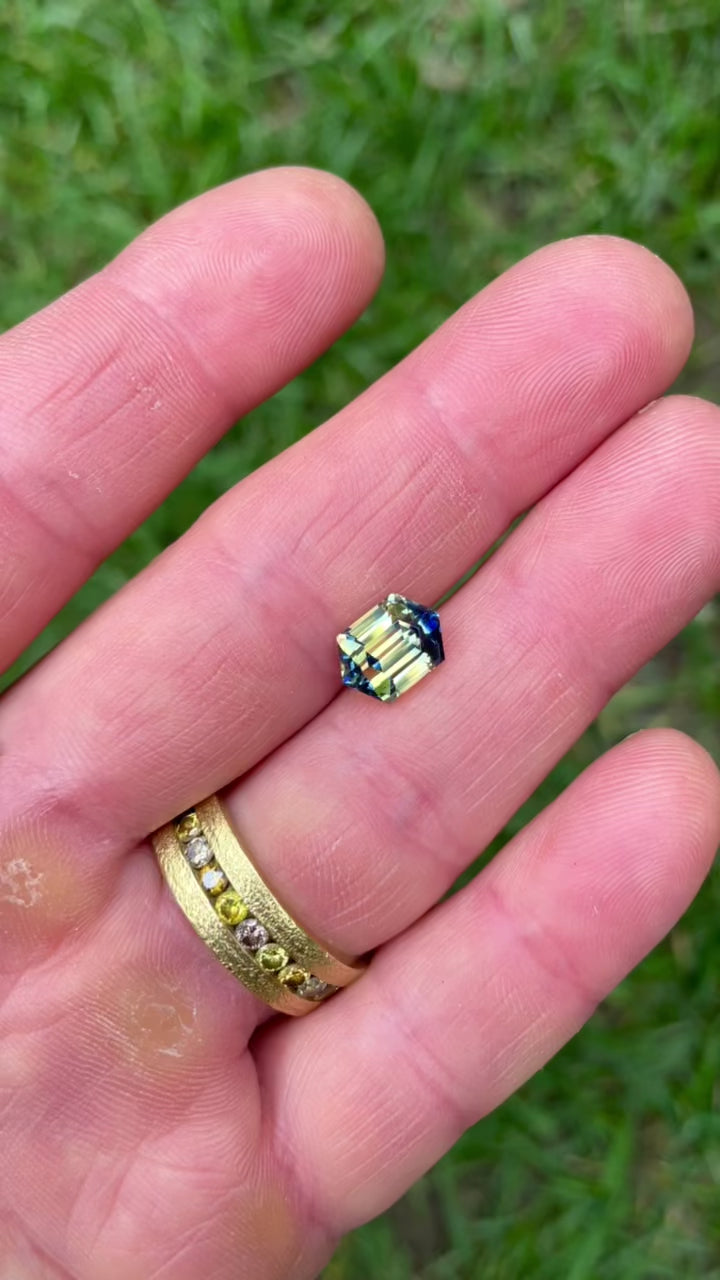 Macro video of an untreated bi-color sapphire, showing radiant transitions between blue, yellow, and green hues in hexagonal step facets.