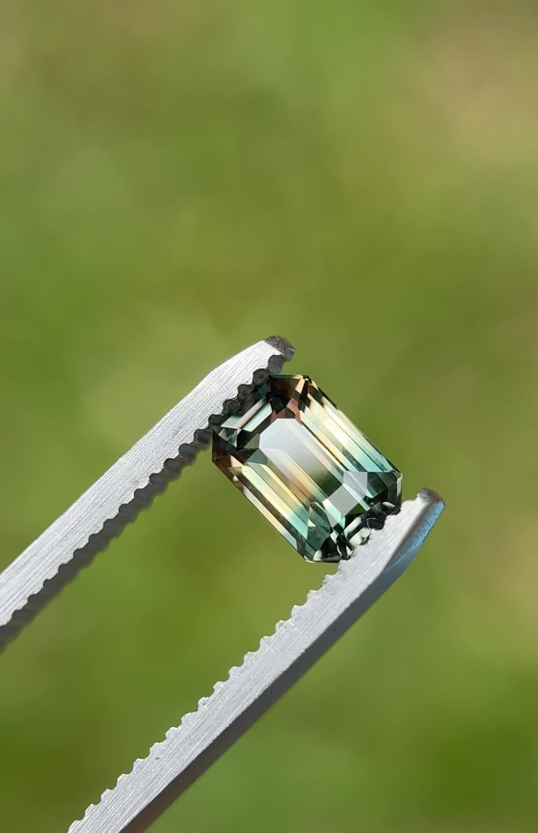 An untreated Madagascar sapphire, 1.60 carats, slowly rotating on a gemstone tray under direct light—highlighting its color-change from lagoon green to earthy pink.