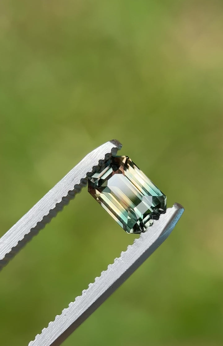 An untreated Madagascar sapphire, 1.60 carats, slowly rotating on a gemstone tray under direct light—highlighting its color-change from lagoon green to earthy pink.